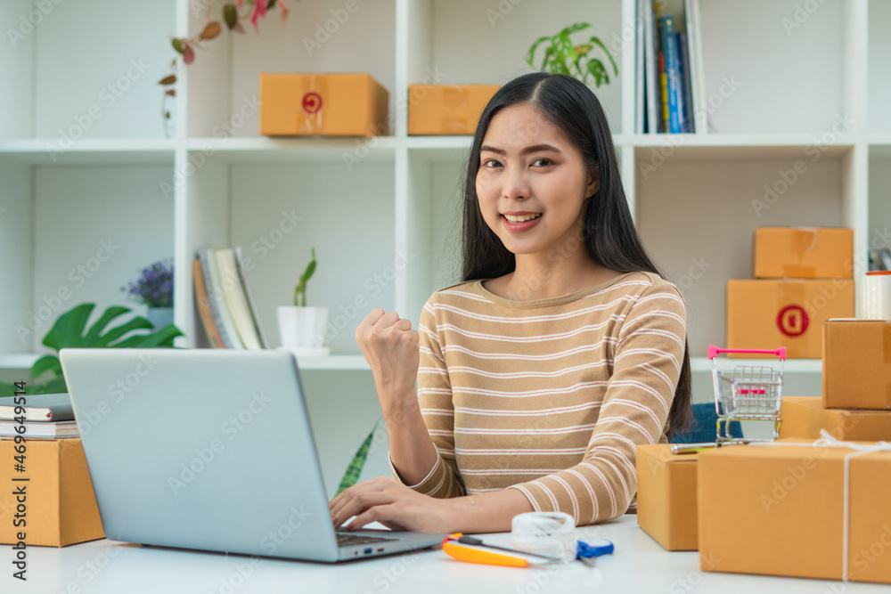 Young asian woman startup small business freelance sitting with parcel box and computer laptop on wo