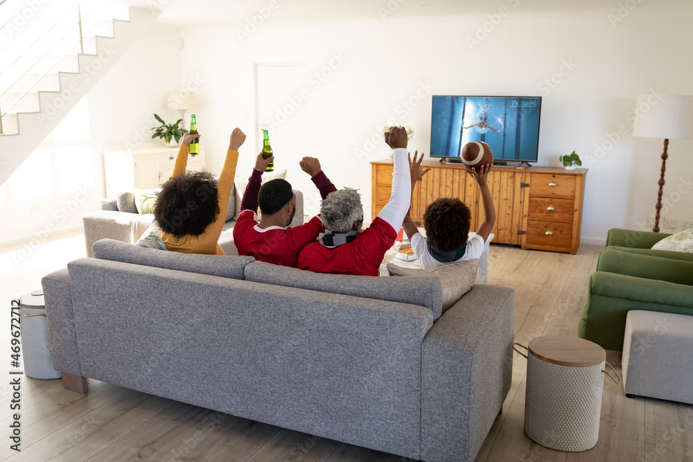 Rear view of family sitting at home together watching swimming competition on tv