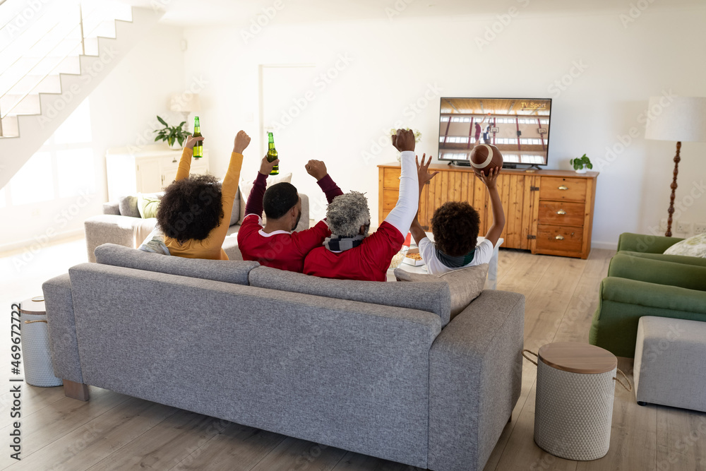 Rear view of family sitting at home together watching basketball match on tv