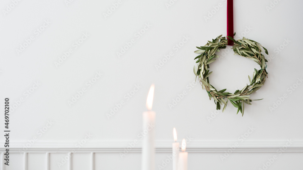 Christmas wreath on a white wall with lighted white pillar candles