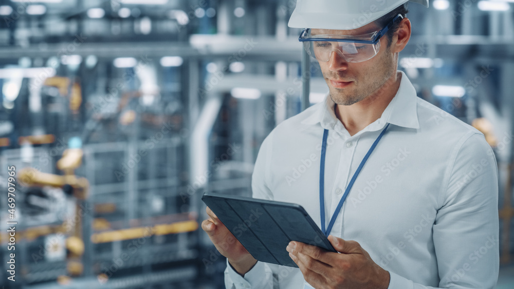 Male Engineer in Safety Goggles and Hard Hat Using Tablet Computer and Looking Out of the Office at 