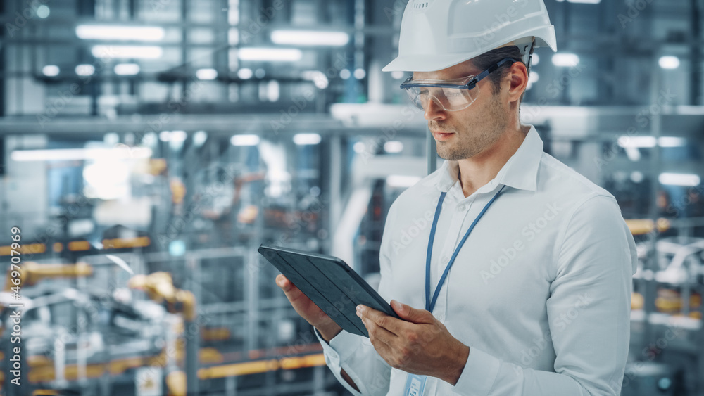 Male Engineer in Safety Goggles and Hard Hat Using Tablet Computer and Looking Out of the Office at 