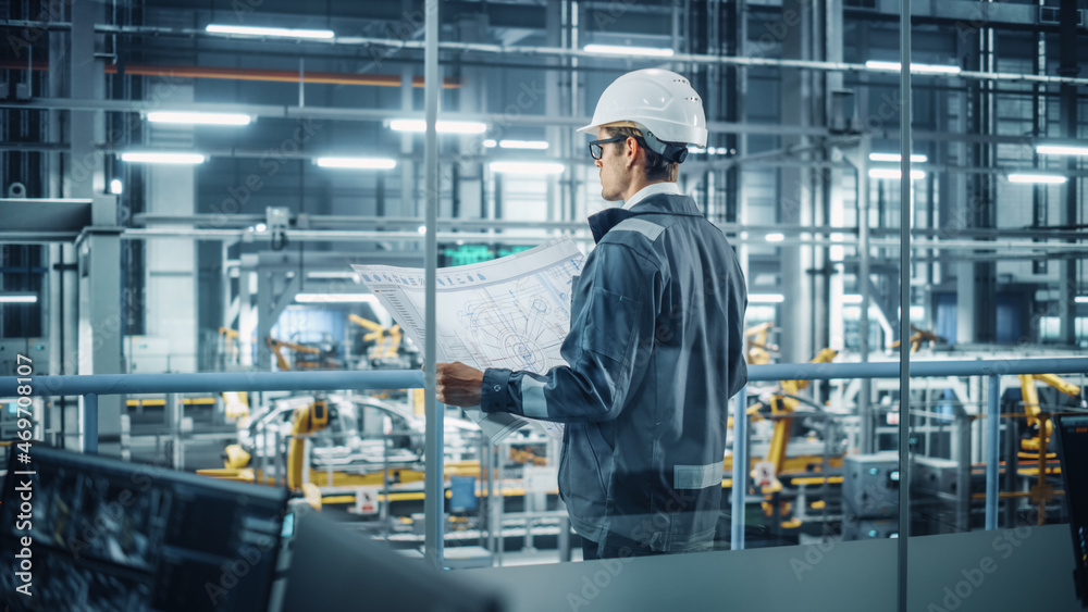 Engineer in Uniform and Hard Hat Looking at a Technical Blueprint at Work in an Office at Car Assemb