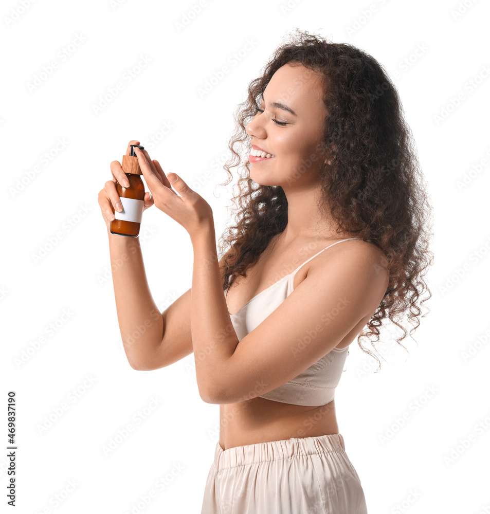 Beautiful African-American woman with cosmetic product in bottle on white background