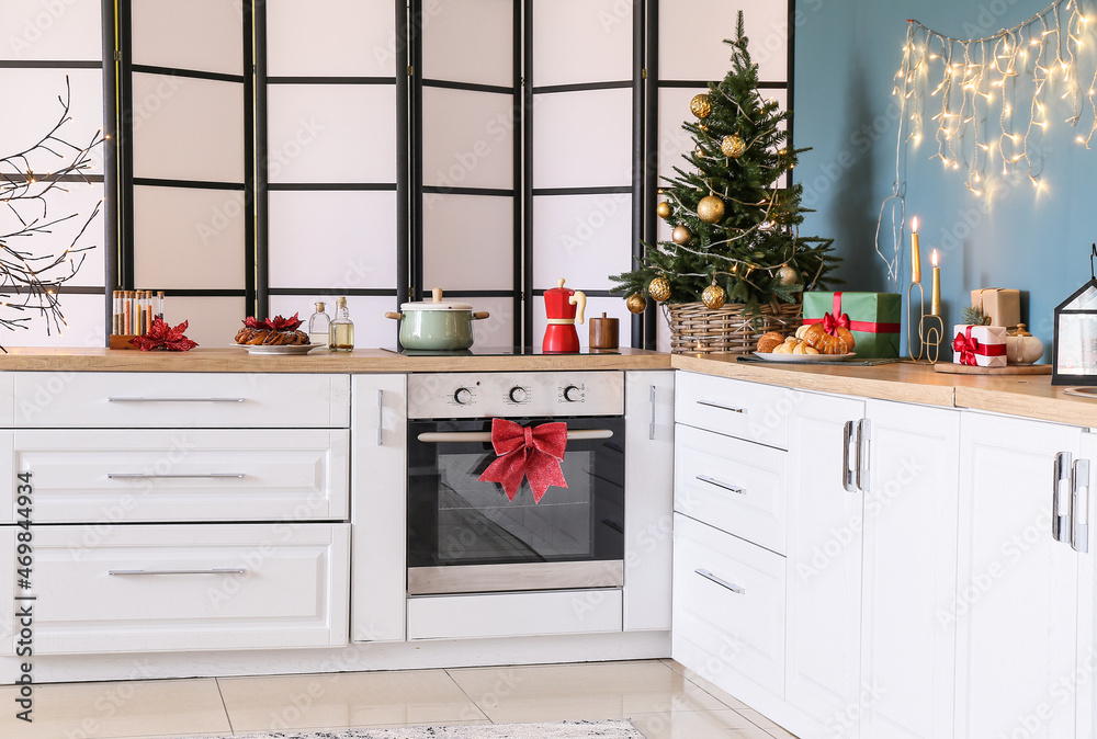 Interior of stylish kitchen with white counters, small Christmas tree and folding screen