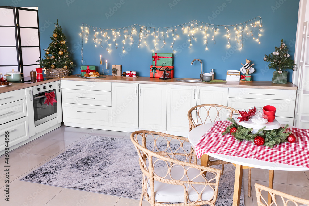 Interior of stylish kitchen with white counters, small Christmas trees and blue wall