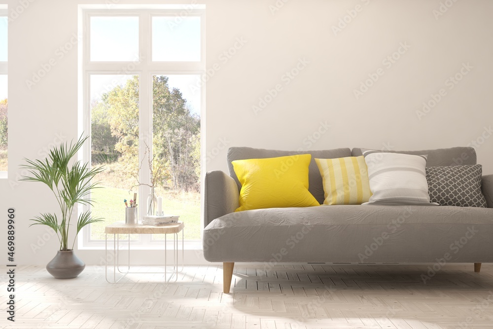 Stylish room in white color with sofa and autumn landscape in window. Scandinavian interior design. 