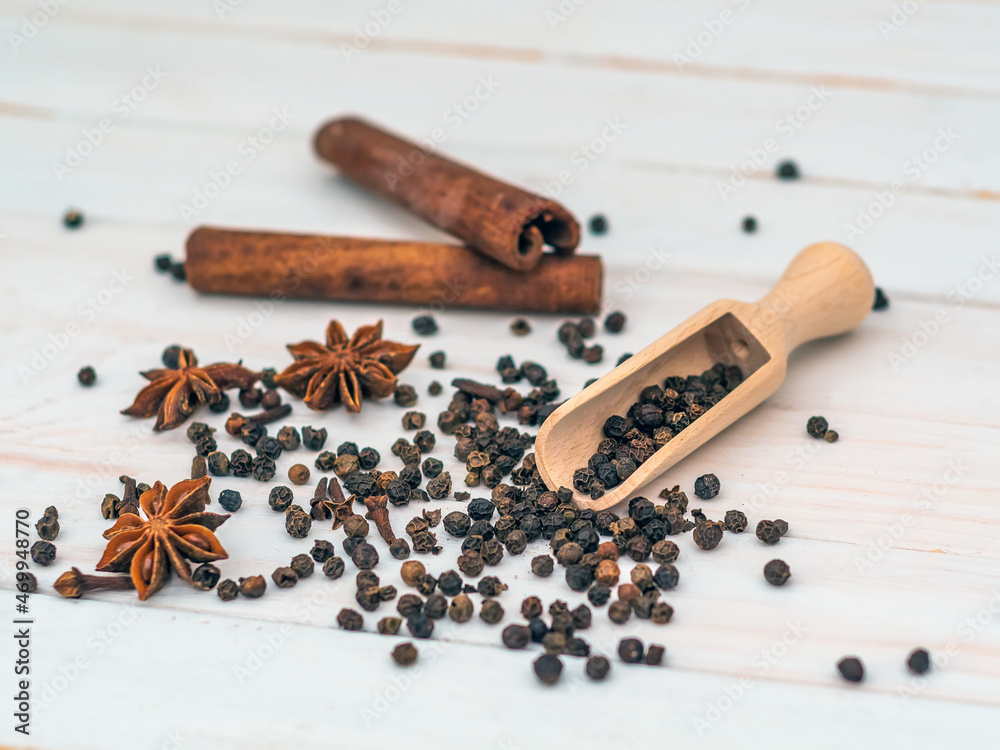 Spices on a background of white planks. Black pepper, cloves, cinnamon, star anise. Close-up.