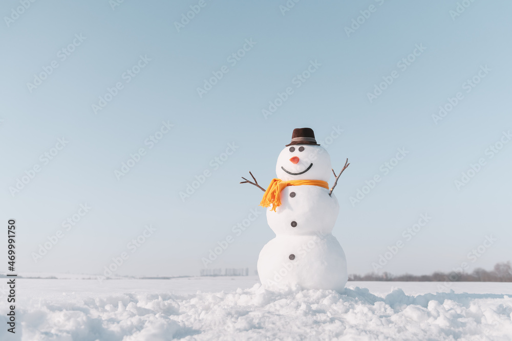 雪地上戴着时尚棕色帽子和黄色鳞片的有趣雪人。背景是蓝天