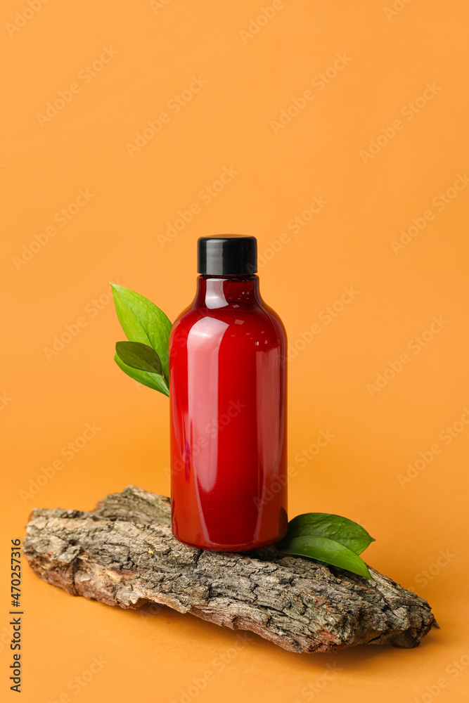 Bottle of shower gel and tree bark on color background