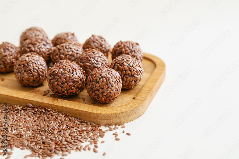 Board with tasty flax seed candies on white background