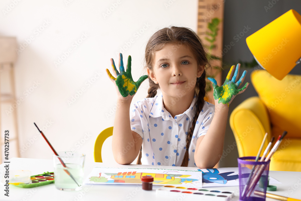 可爱的小女孩在桌子上把手浸在油漆里