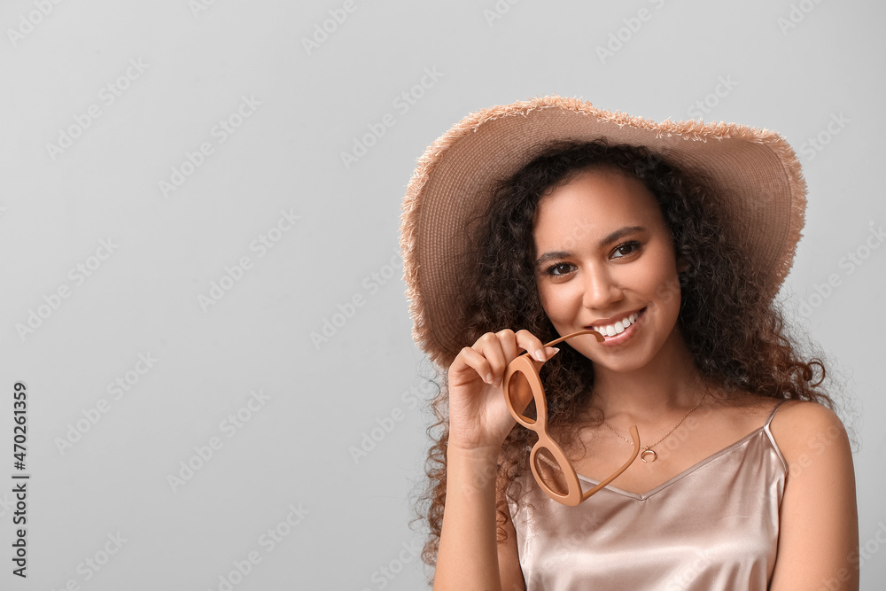 Beautiful African-American woman in broad brim hat on light background