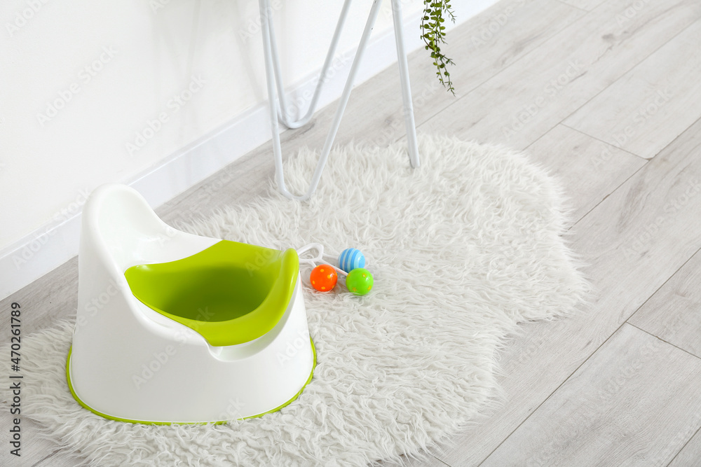 Potty and rattle on grey wooden floor near white wall