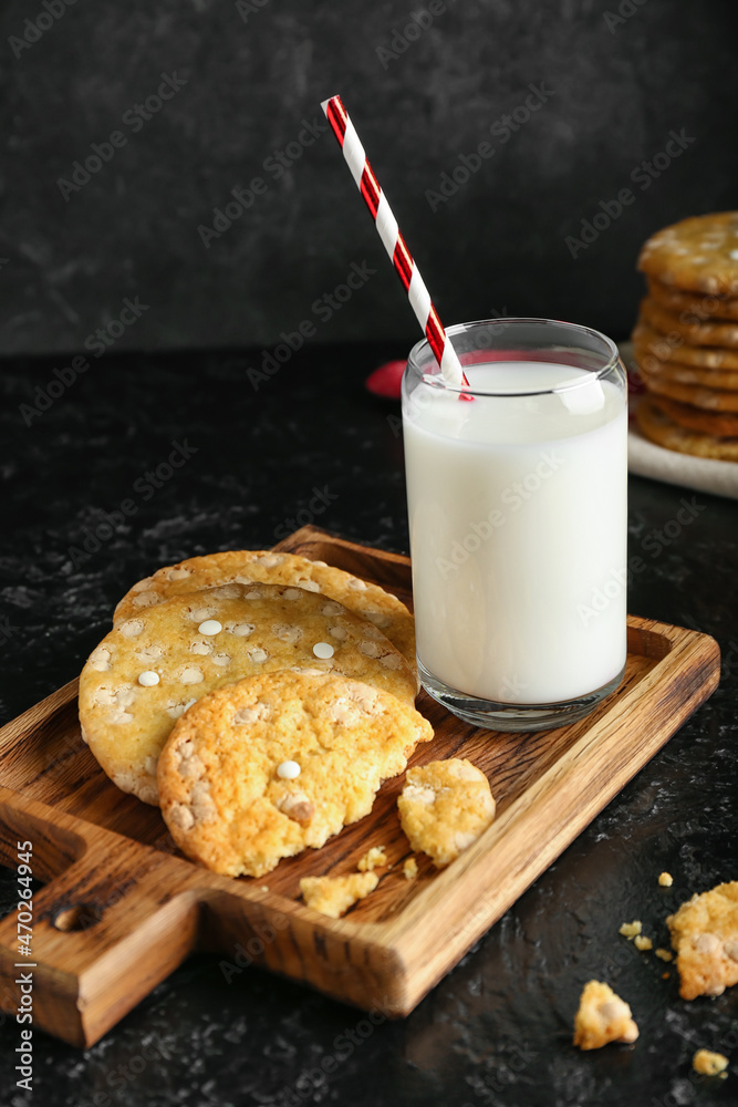 Board with tasty chocolate cookies and glass of milk on dark table