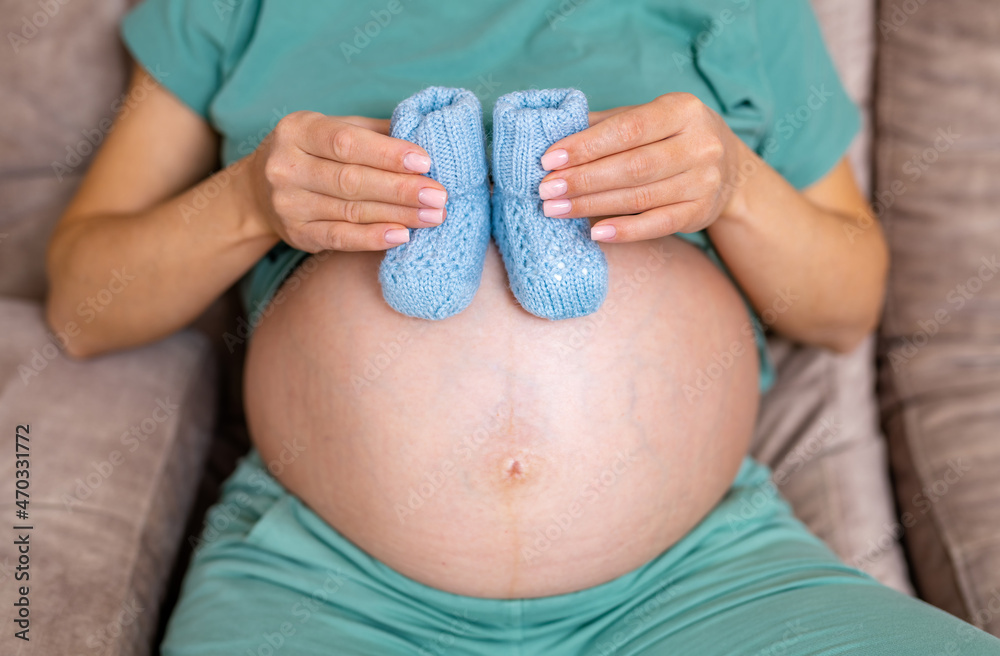 未来的妈妈坐在沙发上，大肚子上抱着婴儿靴。女性抱着新生儿的袜子