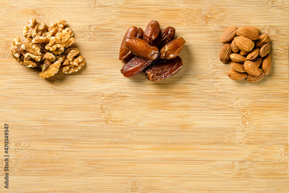 Raw almonds, organic pitted dates and walnut halves on the wooden cutting board background