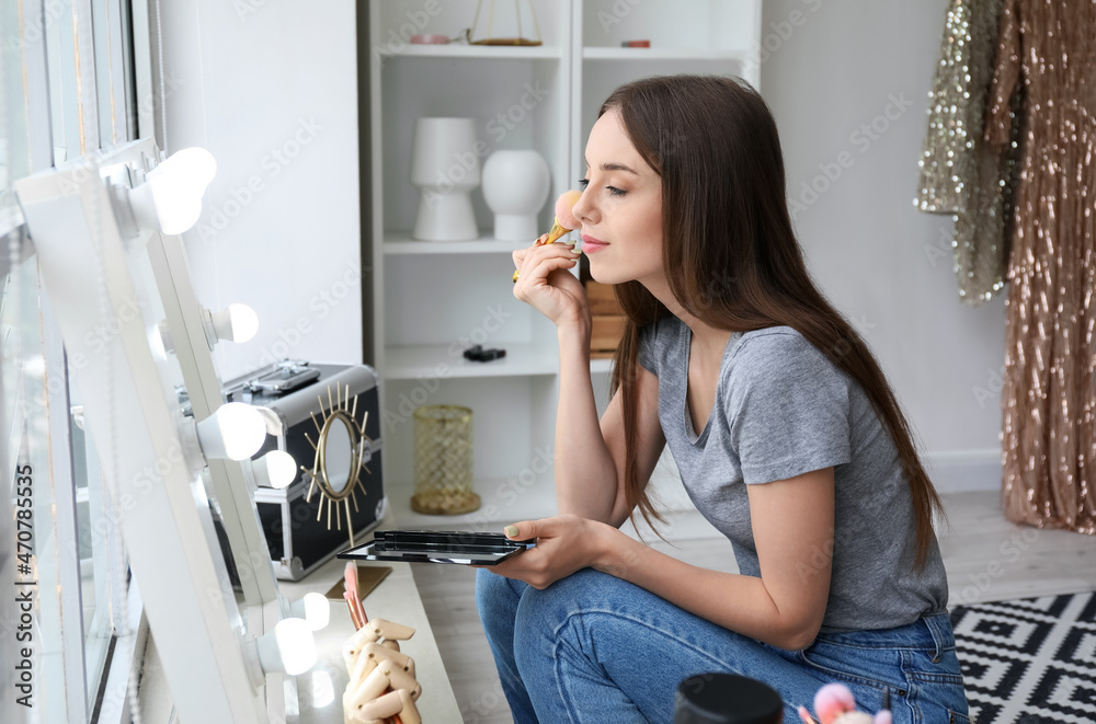 Pretty young woman applying powder with brush near mirror in dressing room