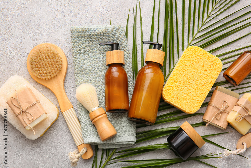 Set of bath supplies with sponges and palm leaf on light background