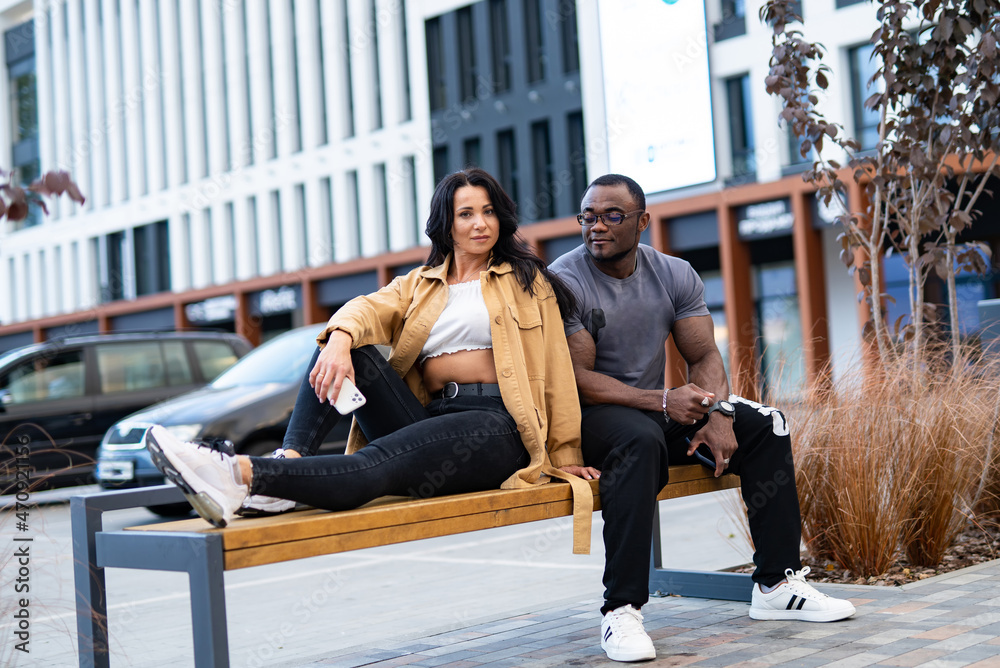 Cheerful young couple sitting outdor on bench. Happy outdoor relationship whaving fun together.