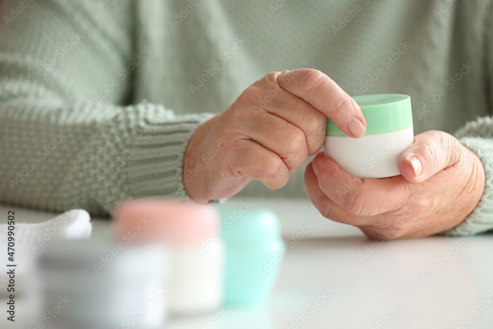 Elderly woman applying cosmetic cream onto her hands at table