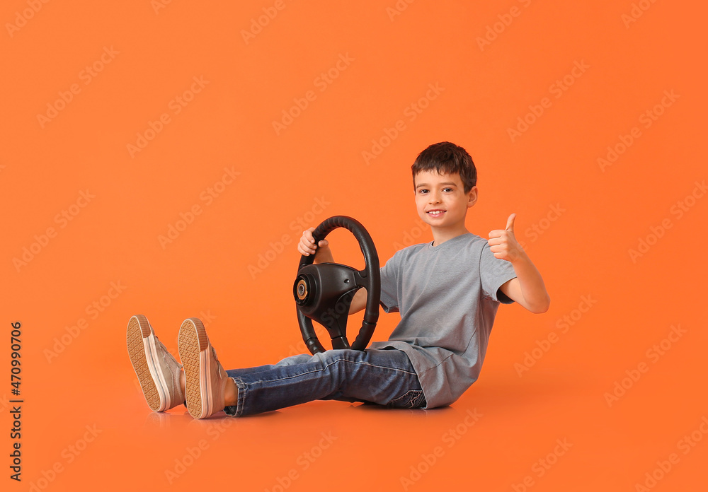 Little boy with steering wheel showing thumb-up on color background