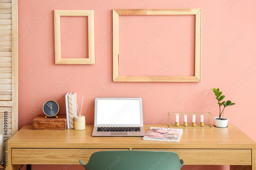 Stylish workplace with laptop and alarm clock in room near wall