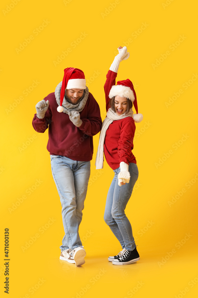 Dancing young couple in stylish winter clothes and Santa Claus hats on color background