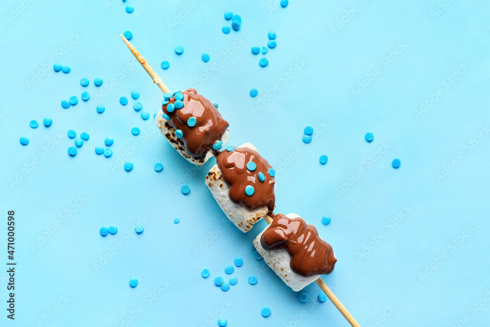 Skewer with tasty grilled marshmallows in chocolate on blue background