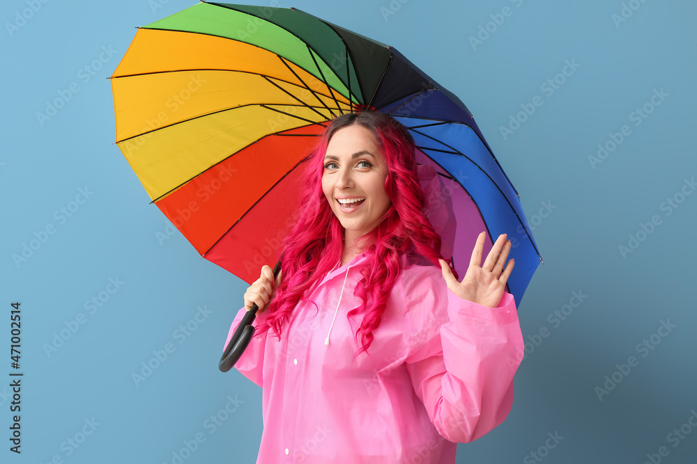 Beautiful woman in raincoat and with umbrella on color background