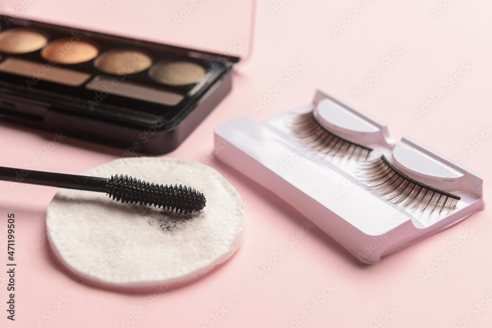 Eyeshadows, mascara, false eyelashes and used cotton pad on pink background, closeup