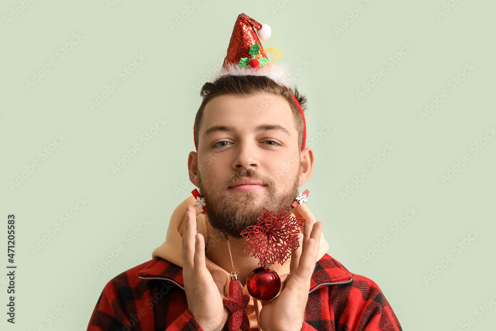 Young man in stylish winter clothes and with Christmas decor on light background