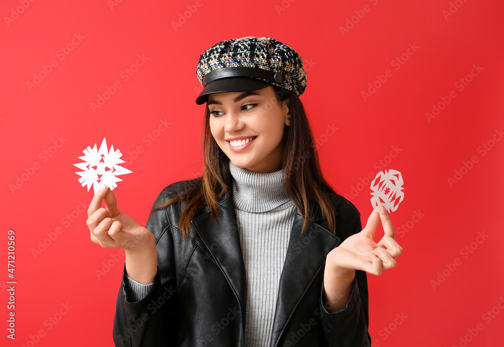 Beautiful woman in cap with paper snowflakes on red background