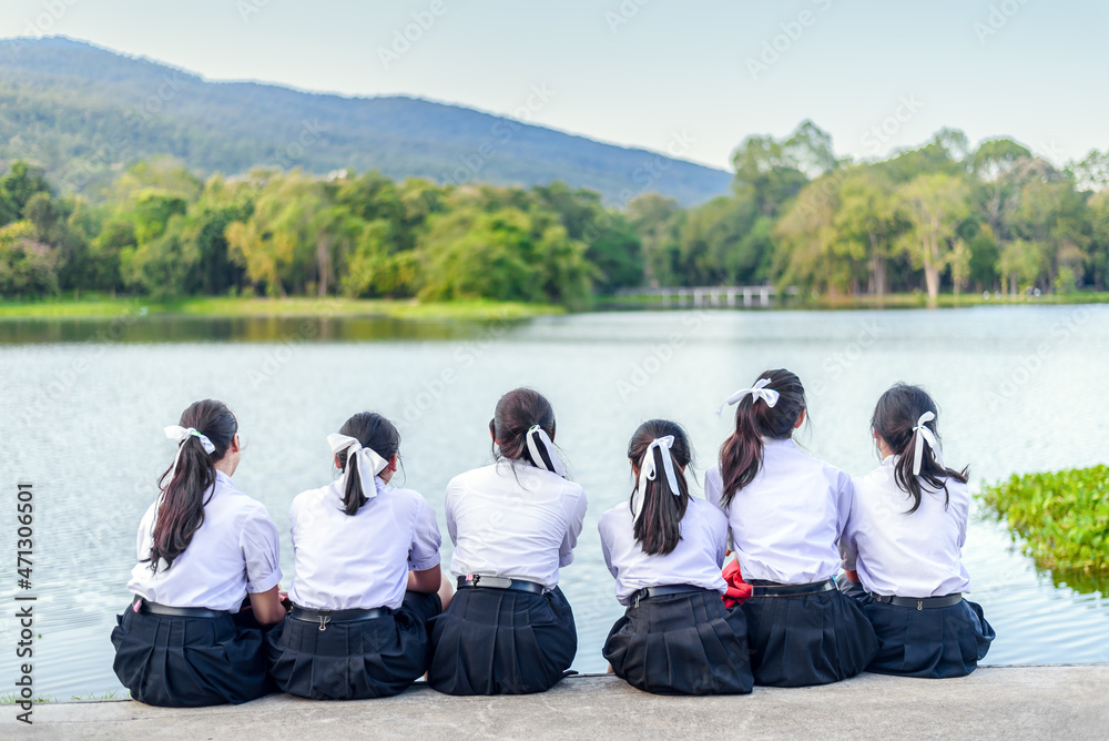 一群泰国学生女孩朋友穿着制服坐在户外湖边