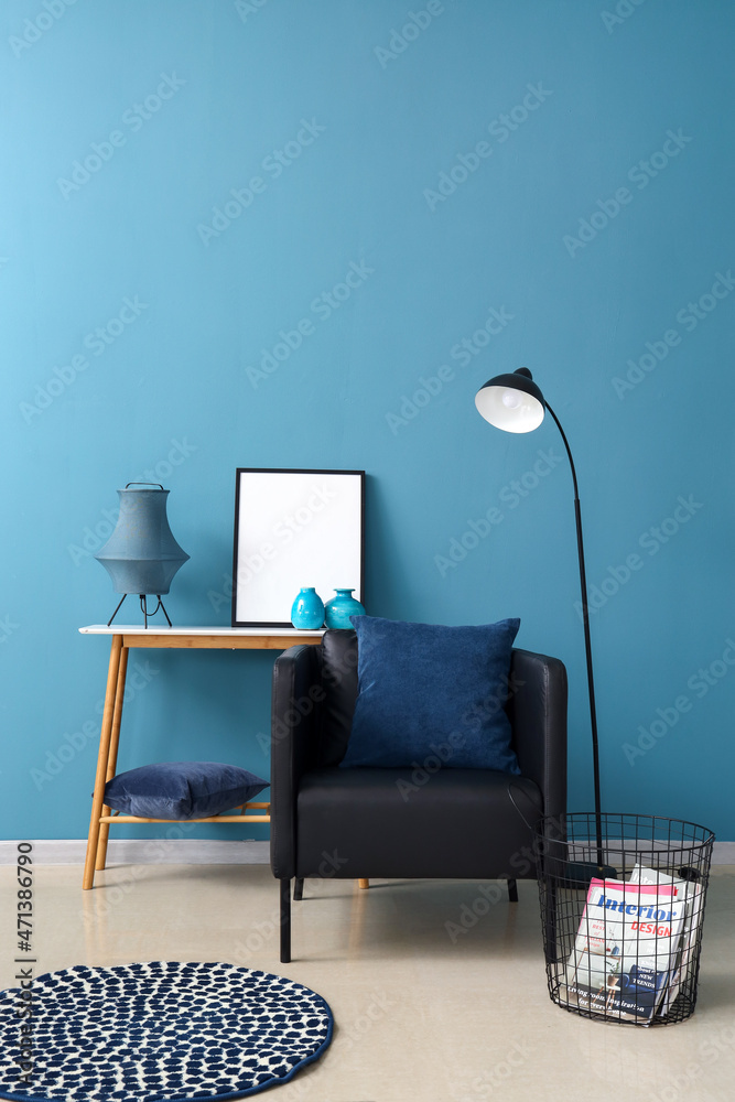 Modern armchair, table with blank frame and floor lamp near color wall