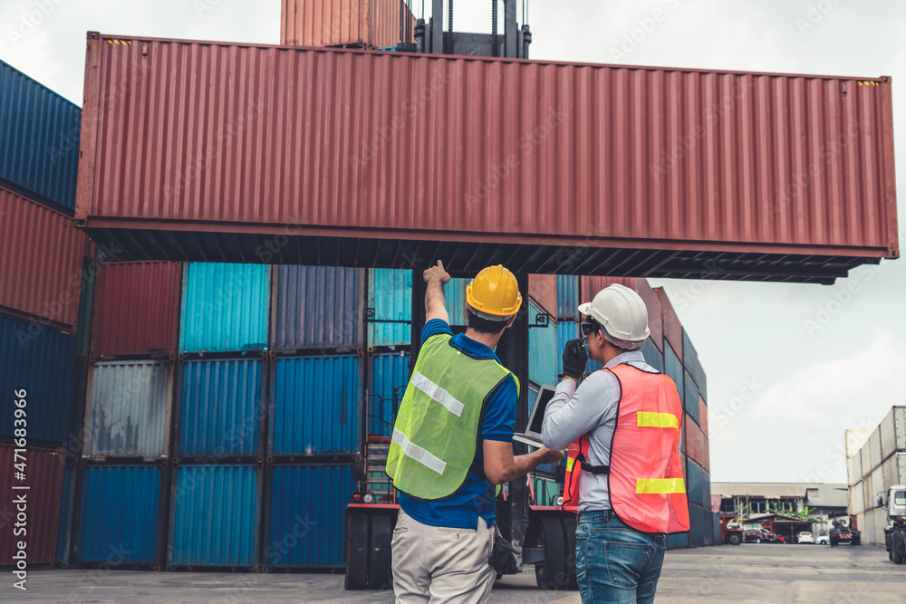 Industrial worker works with co-worker at overseas shipping container yard . Logistics supply chain 