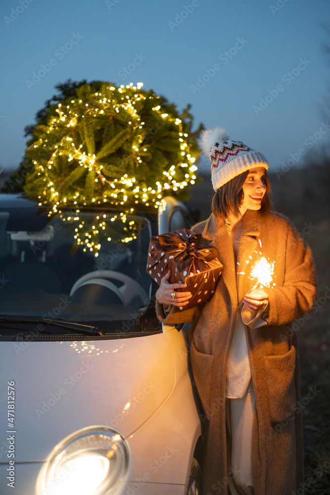 黄昏时，一位快乐的高加索妇女在汽车附近燃放烟花，圣诞树在大自然中。ce的概念