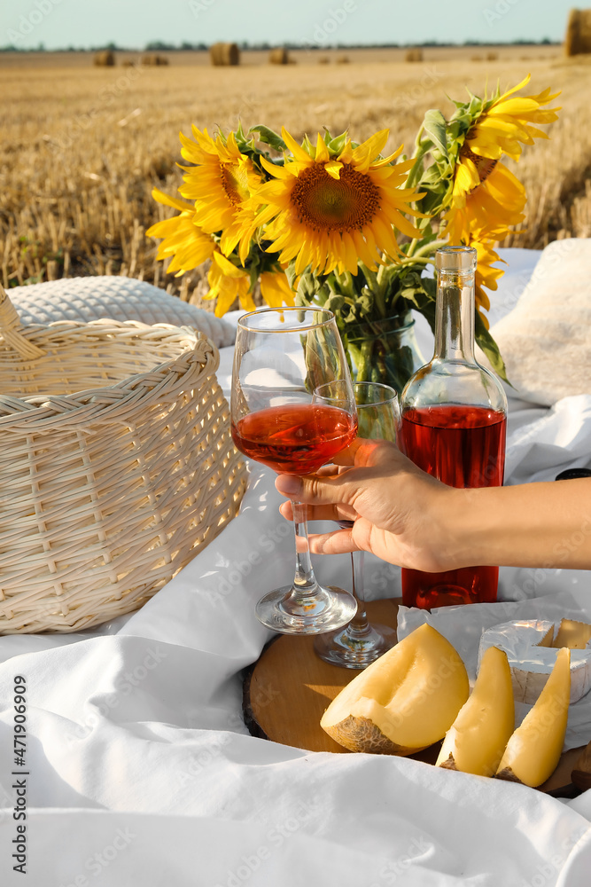 Young woman having romantic picnic with fruits and wine on harvested field background