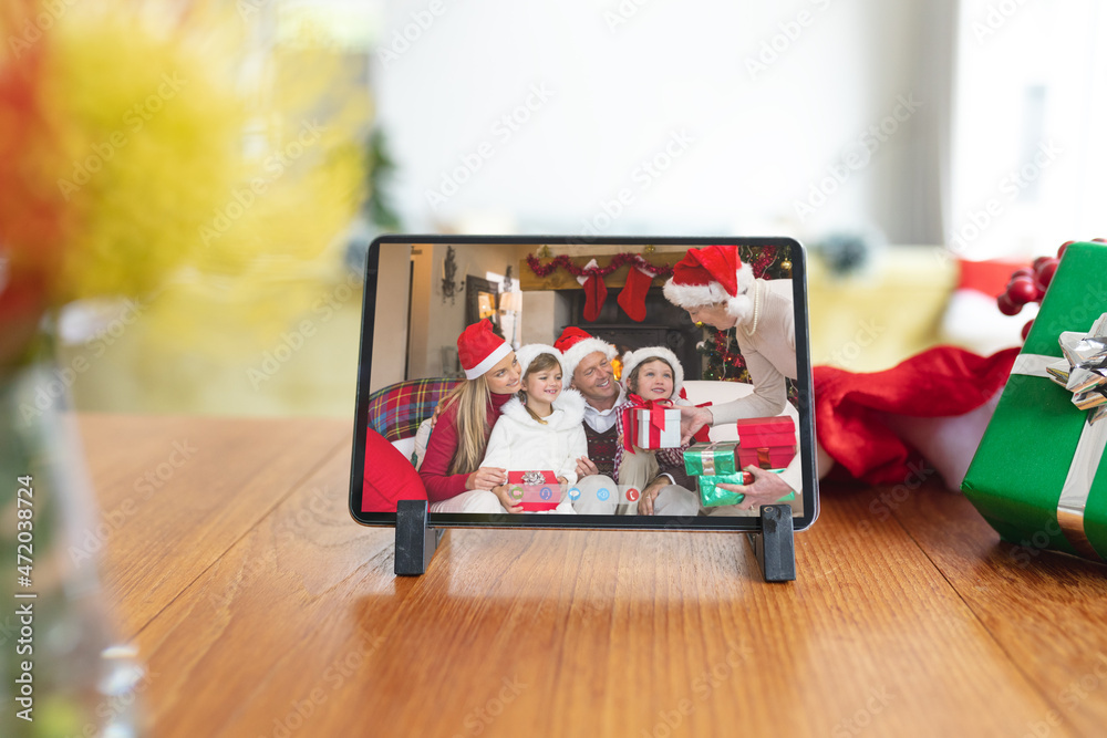 Happy caucasian family in santa hats giving presents on tablet video call screen at christmas time