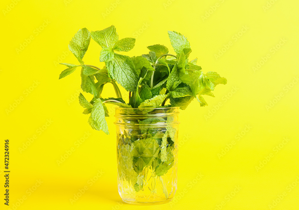 Glass jar with bunch of mint on yellow background