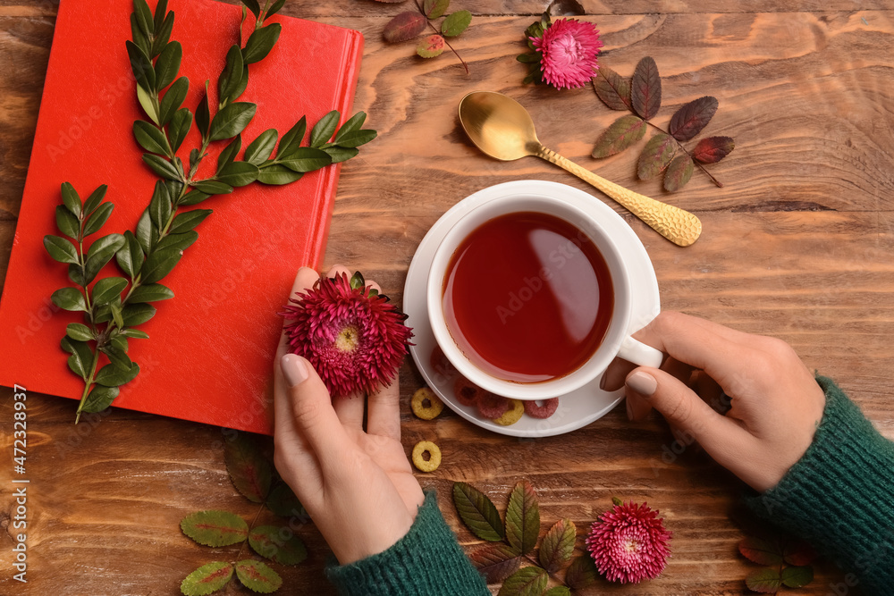 女性手拿着一杯茶，笔记本和木背景紫荆花，特写