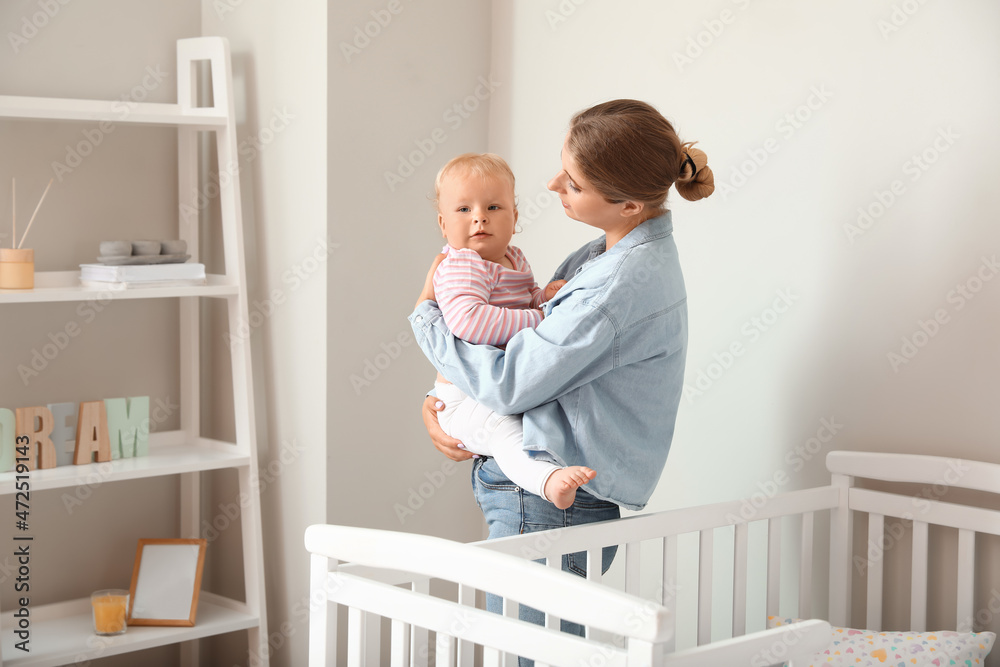 Young mother holding her little baby near crib in bedroom