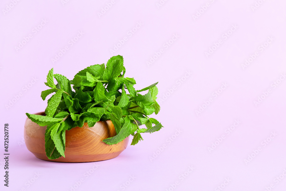 Bowl with fresh mint on lilac background