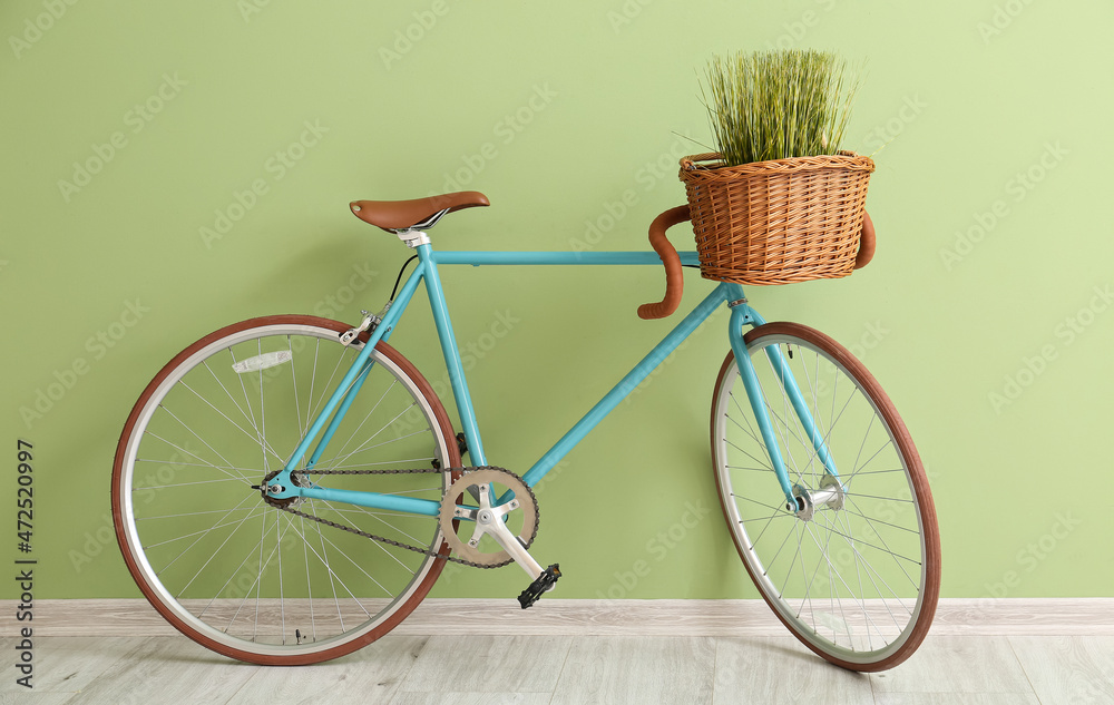 Stylish bicycle with wicker basket and grass near green wall