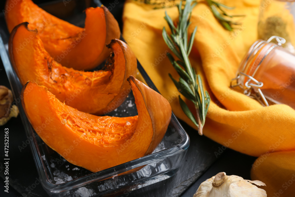 Dish with baked pumpkin pieces on black background