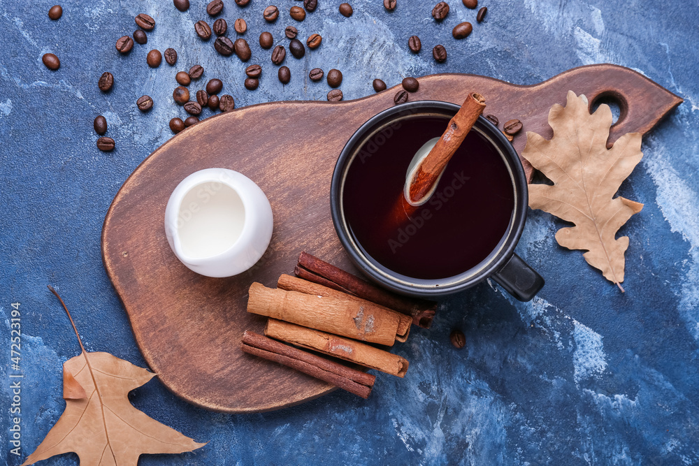 Cup of tasty coffee with cinnamon and beans on blue background