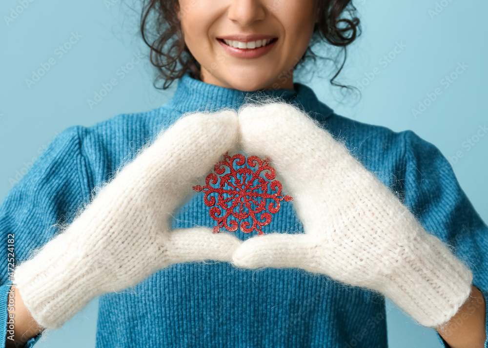 Beautiful smiling woman holding red snowflake on blue background, closeup