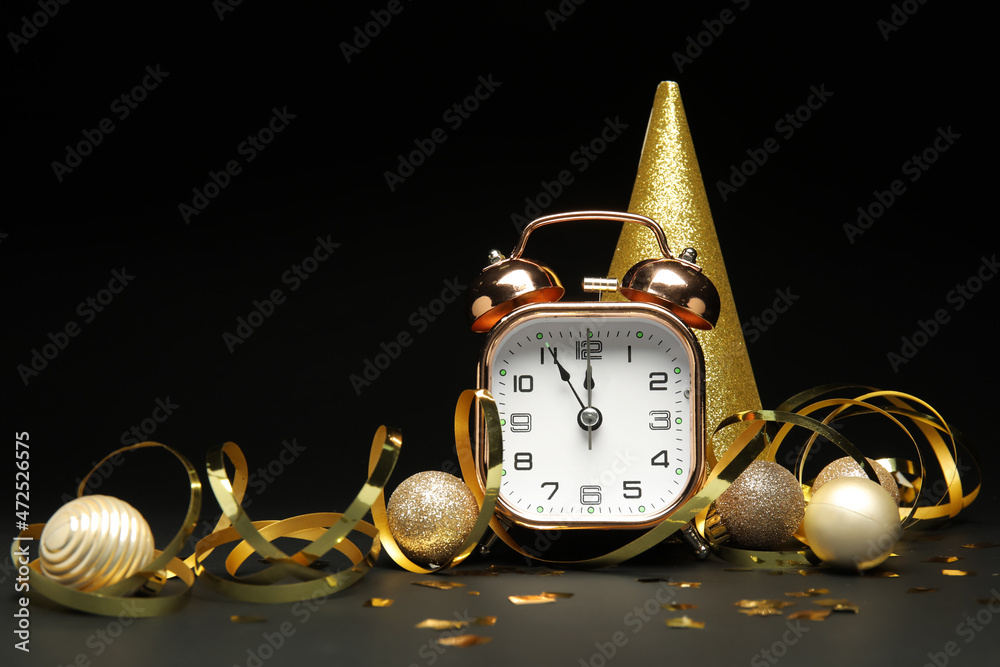 Alarm clock, party hat and Christmas decorations on dark background