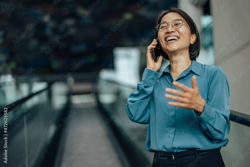 微笑的亚洲女人，在使用电话时大声大笑