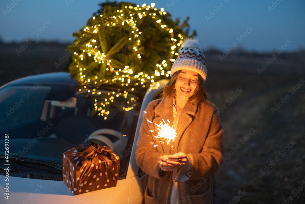 黄昏时，一位快乐的高加索妇女在汽车附近用圣诞树向大自然发射烟花。ce的概念